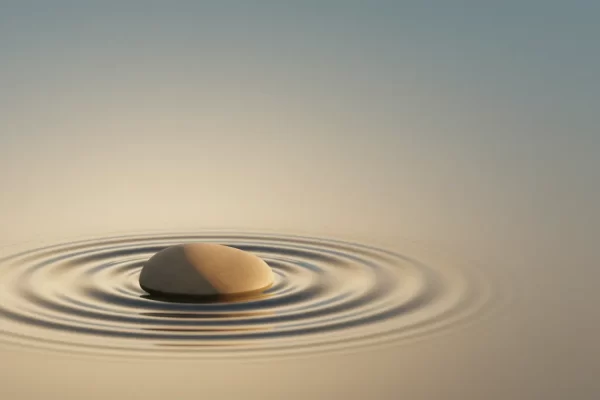 Single smooth stone in still water with gentle ripples under warm light on a soft, neutral background.